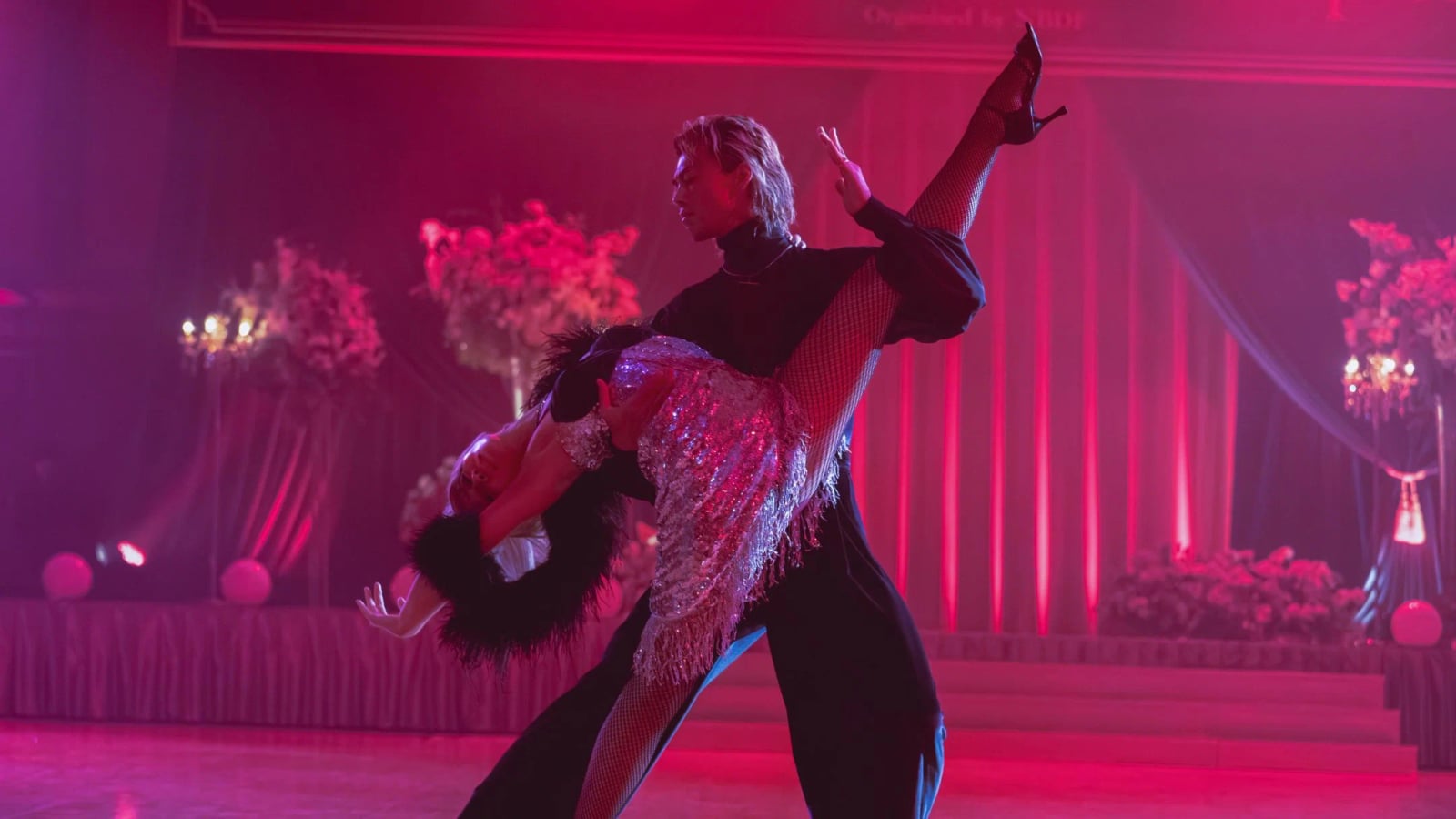 Zwei Männer in Tanzhaltung stehen sich intensiv gegenüber, die Stirnen nah beieinander, in eleganter Ballroom-Kleidung.