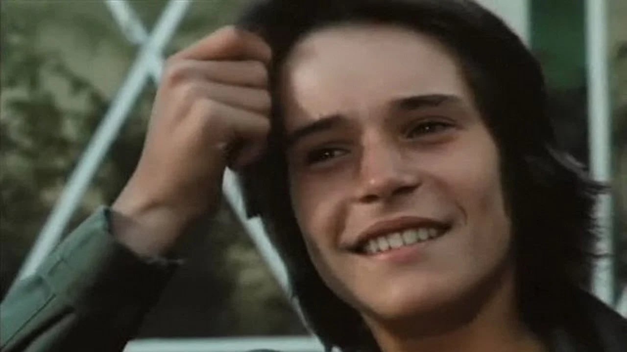 Ein junger Junge in blauer Jeans blickt nachdenklich zur Seite, Szenenbild aus dem französischen Jugendfilm Erste Versuchungen von 1977