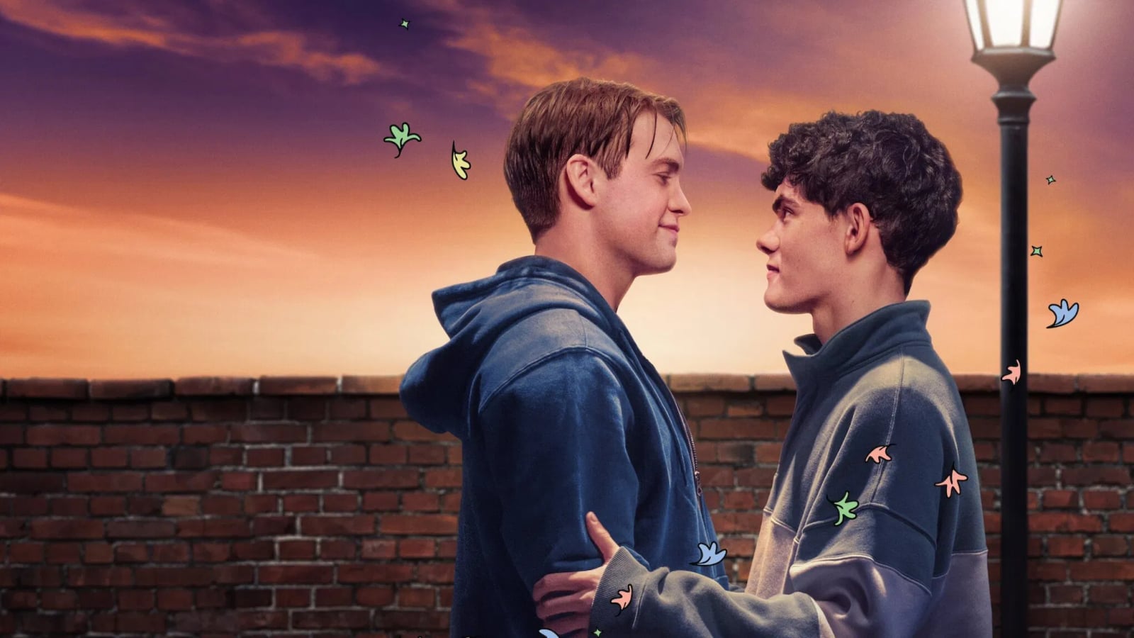 Joe Locke als Charlie Spring und Kit Connor als Nick Nelson sitzen nebeneinander und lächeln sich an in einer Szene aus der Netflix-Serie Heartstopper