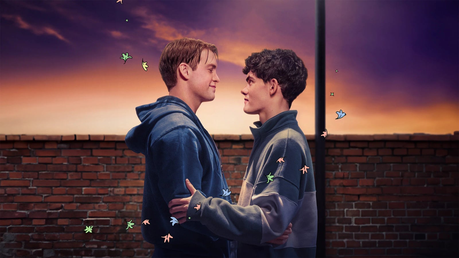 Joe Locke als Charlie Spring und Kit Connor als Nick Nelson sitzen nebeneinander und lächeln sich an in einer Szene aus der Netflix-Serie Heartstopper