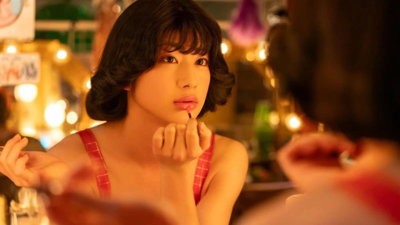 Haruki Mochizuki als Ai Haruna in einer schillernden Bühnen-Szene, umgeben von bunten Lichtern und Cabaret-Atmosphäre.